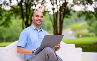 Image of man smiling, working at a laptop outside