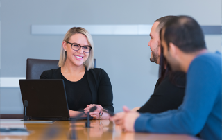 three employees sitting at a table. woman smiling towards camera